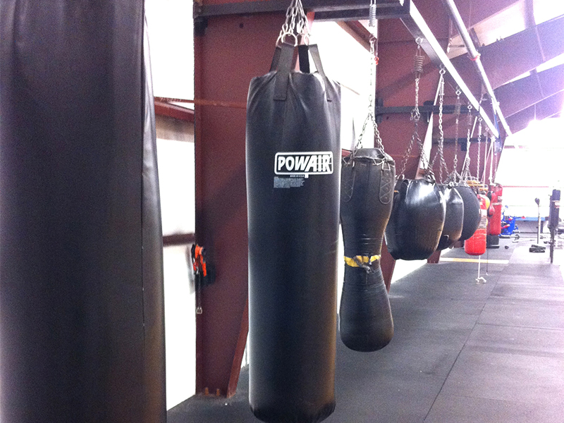 two black boxing bags hanging from hooks in a gym