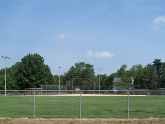 a baseball field with a fence and trees in the background