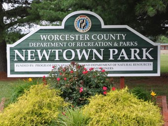 a sign for a town park with flowers in the foreground