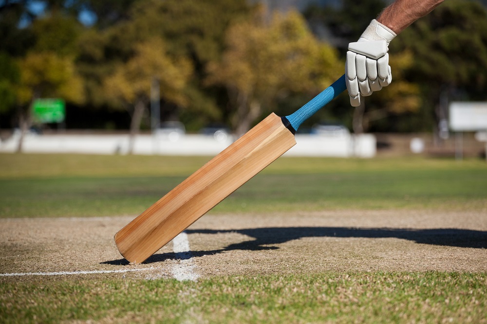 a person holding a wooden cricket bat on top of a field