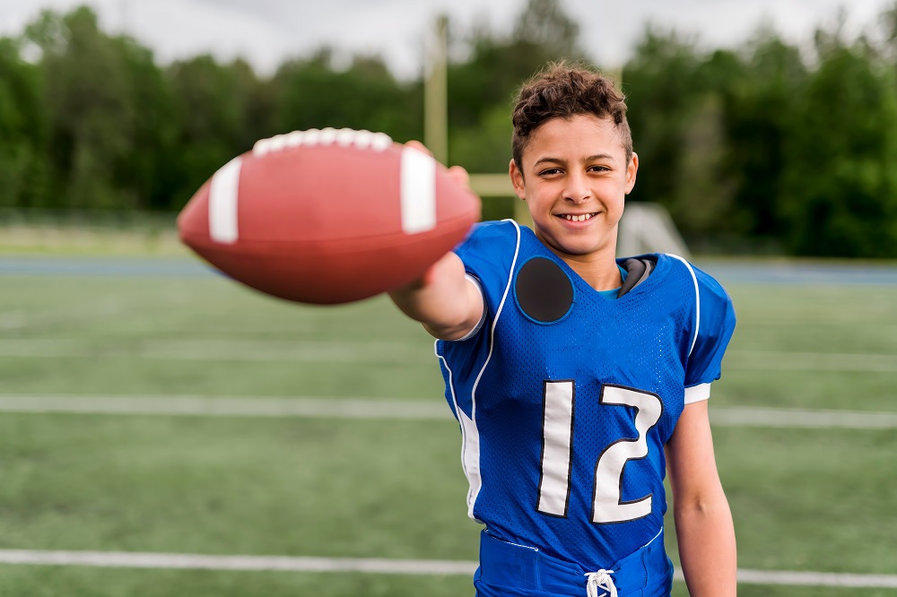 a young boy holding a football on top of a field