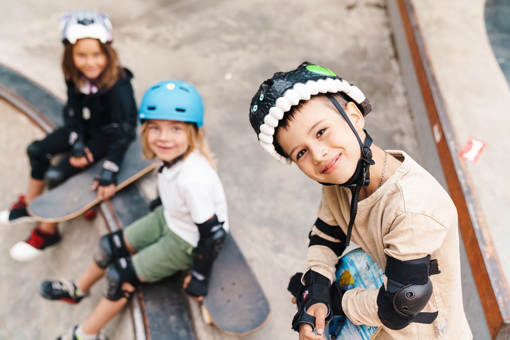 three children with helmets and skateboards sitting on stairs