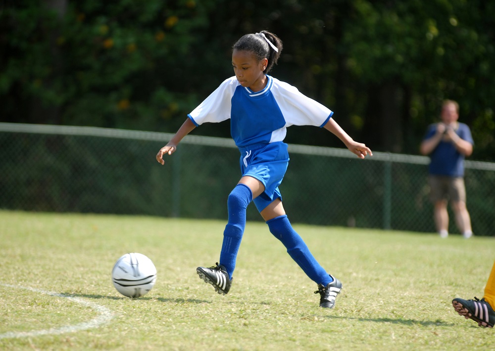 a young girl kicking a soccer ball on a field